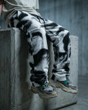 Person sitting on a concrete block wearing Noir Visage Wide Leg Trousers with a monochromatic graphic design.