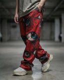 Ocular Crimson Wide Leg Trousers with eye graphics worn by a model in a concrete setting.